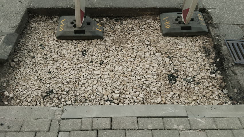 A pile of gravel on the sidewalk by a drain near the road surface