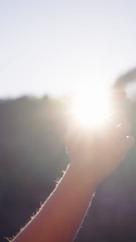 Vertical. Hand unrecognizable Caucasian person reaches toward sun in a longing gesture raising his arm toward the sky. Playing with sunlight between fingers in forest. Thoughts alone enjoying nature