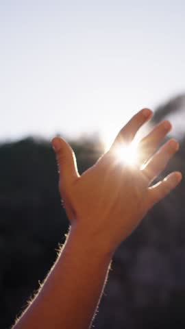 Vertical. Hand unrecognizable Caucasian person reaches toward sun in a longing gesture raising his arm toward the sky. Playing with sunlight between fingers in forest. Thoughts alone enjoying nature