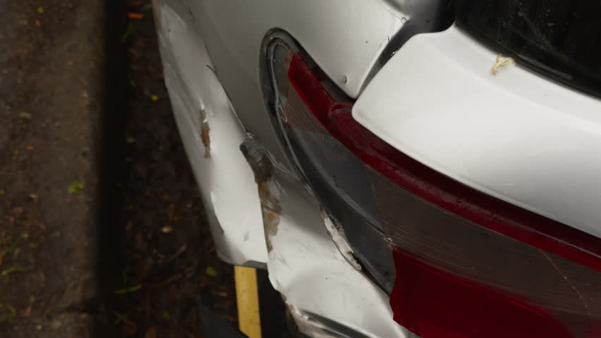 White car with a damaged bumper parked on roadside