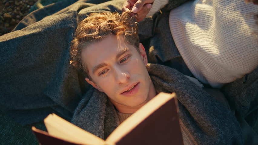 Attractive tranquil man lying woman knees enjoying romantic picnic closeup. Curly boyfriend reading book aloud for relaxed girlfriend on nature. Cute happy couple relaxing at weekend in ocean evening - Powered by Shutterstock - Get 15% off with code: PIKWIZARD15