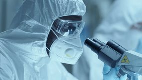 African American male chemist wearing protective coverall suit, face mask, safety glasses and gloves using microscope during medical test in laboratory. Zoom shot, close-up view - Powered by Shutterstock - Get 15% off with code: PIKWIZARD15