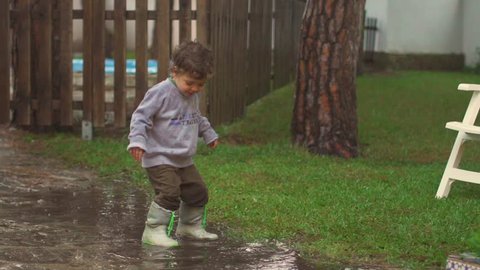 Slow motion of happy child playing, jumping and smiling under the rain