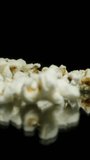 Vertical video. A handful of popcorn is poured out of the hand onto the black background. Macro slow motion.