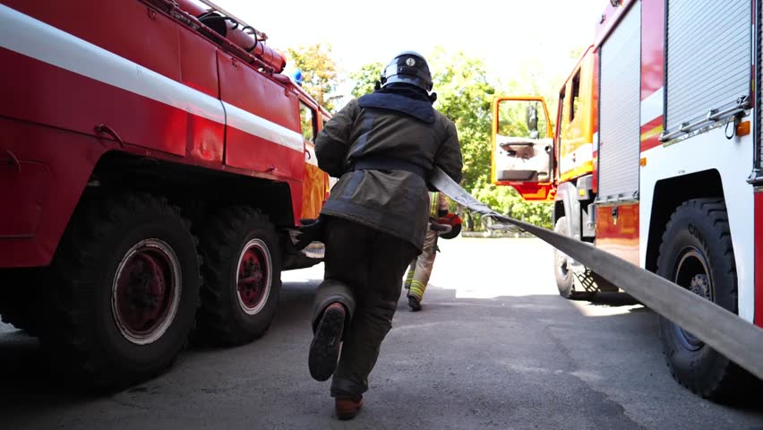 Young male firefighters with equipments running to extinguish fire. Professional fireguards jogging to the place of emergency. Concept of saving lives and heroic profession. Close up Slow motion