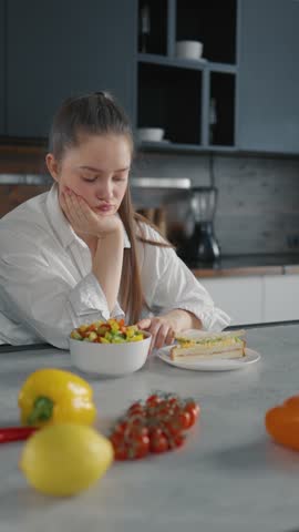 Pensive woman choose healthy food on diet. Obese girl chooses between a sandwich and vegetables, makes healthy decisions, and forms healthy habits. Healthy unhealthy food, weight loss concept.