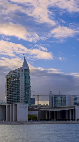 Beautiful clouds fly over famous twin residential buildings San Rafael and San Gabriel in Park of Nations area, Lisbon, Portugal. Riverfront walkway with Pavilion of Portugal and modern architecture