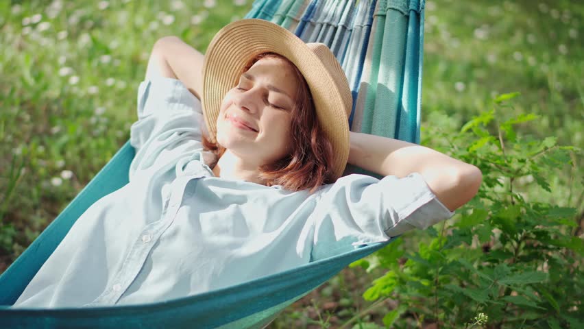 A young Caucasian woman in a hat chilling in a hammock in the spring garden