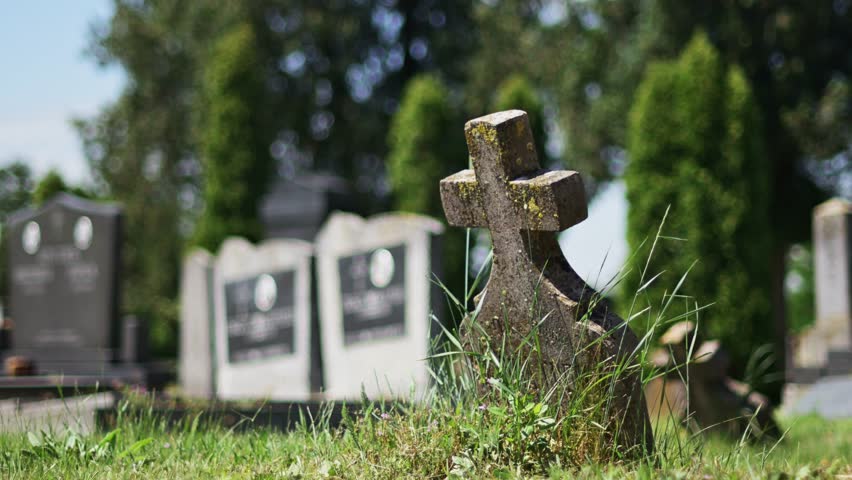 Old concrete christian cross tombstone on a graveyard burial ground, selective focus