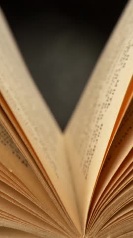 Camera moves through opened vintage book. Old book lying with their pages open. Black background. Slider vertical shot