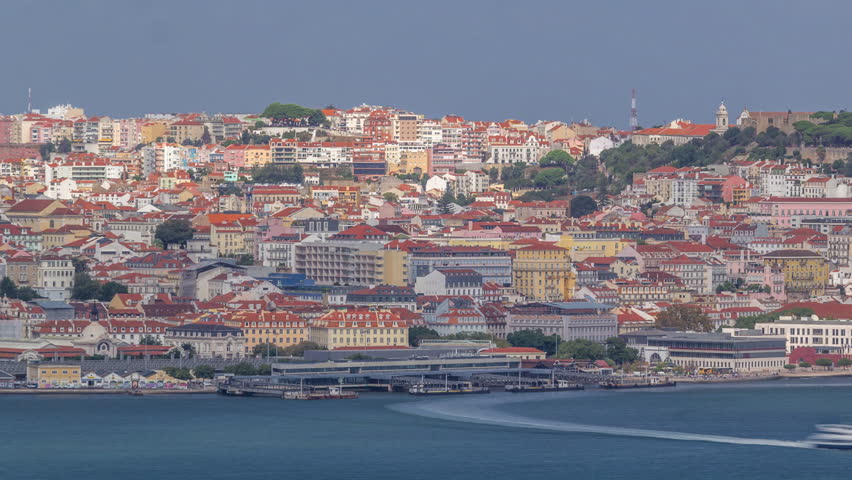 Aerial view of Lisbon over Tagus river from viewpoint of Cristo Rei in Almada with yachts tourist boats timelapse. Historic district with red roofs. Castle on the top. Lisbon, Portugal