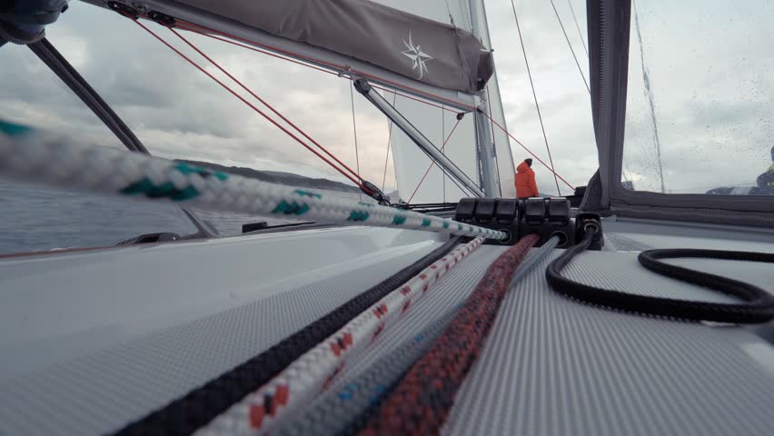 Journey through the cold sea in Norway by sailing yacht. POV shot. White sails of boat are fluttering in the wind during fast movement. Captain holds the helm of the ship. Magnificent seascape