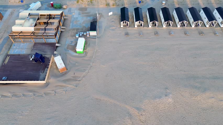 Beautiful flight in summer over the beach in Katwijk aan Zee. People are resting near the sea. Houses for tourists. Beach umbrellas, rides, people swimming in the sea. Beach in Netherland. North Sea.