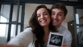 Caucasian family smiling happy laughing pregnant couple smile laugh woman pregnancy man female male guy girl hugging kissing cuddling showing demonstrate ultrasound image picture at home excited baby - Powered by Shutterstock - Get 15% off with code: PIKWIZARD15