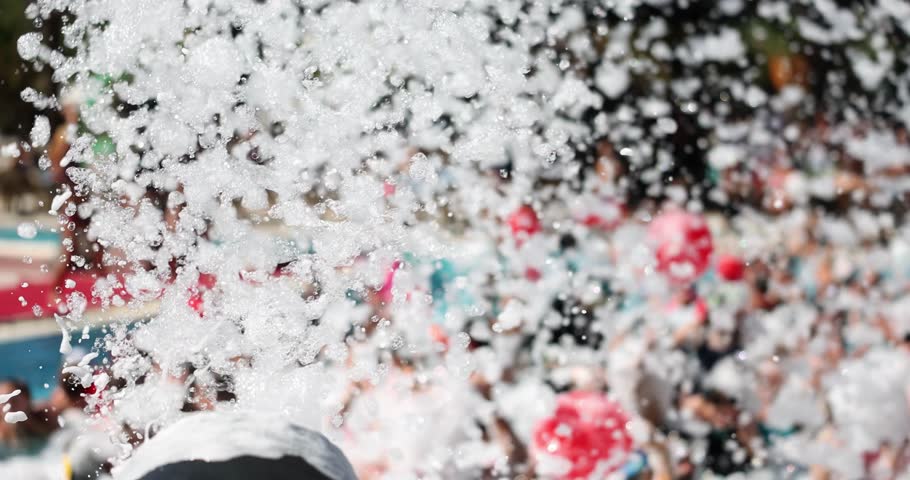 Automatic foam machine shoots with froth at poolside foam party in daytime. Mechanical equipment for fun holidays. Wet fluffy substation producing slow motion
