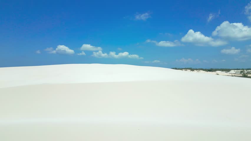 Lady in red dress on white sand dunes in Brazil desert in Parque Nacional dos Lencois Maranhenses. Attractive young woman in red dress. Aerial drone view.