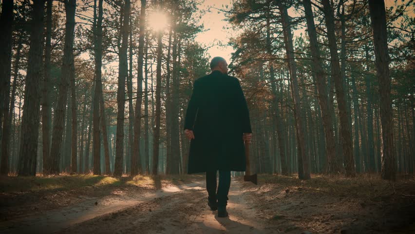 Killer in forest, maniac wearing coat with axe in hands walking between trees in foggy forest, looking around. Bloodthirsty criminal maniac carrying case, searching for victim