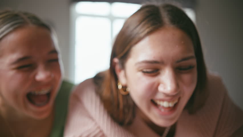 Close up shot of two teenage girls with one wearing orthodontic braces laughing and having fun looking at social media post or streaming online on mobile phone in bedroom at home - shot in slow motion