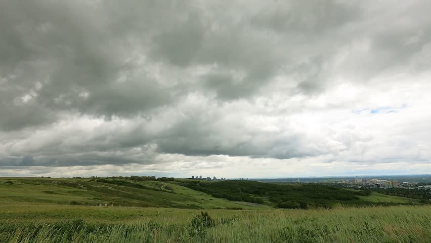 Stormy clouds travel fast above green hill grassland or parks in Alberta Canada. timelapse rainy season wet weather in the summer. beautiful landscape background of the nature. Amazing God