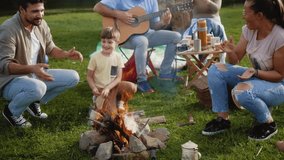 Multigenerational cheerful family singing and playing guitar by the campfire on a summer family camping trip in nature - Powered by Shutterstock - Get 15% off with code: PIKWIZARD15