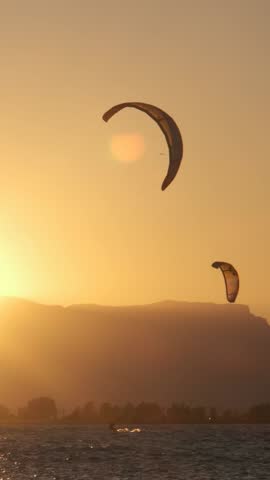 Unrecognizable man kite surfing at sunset against the sunlight