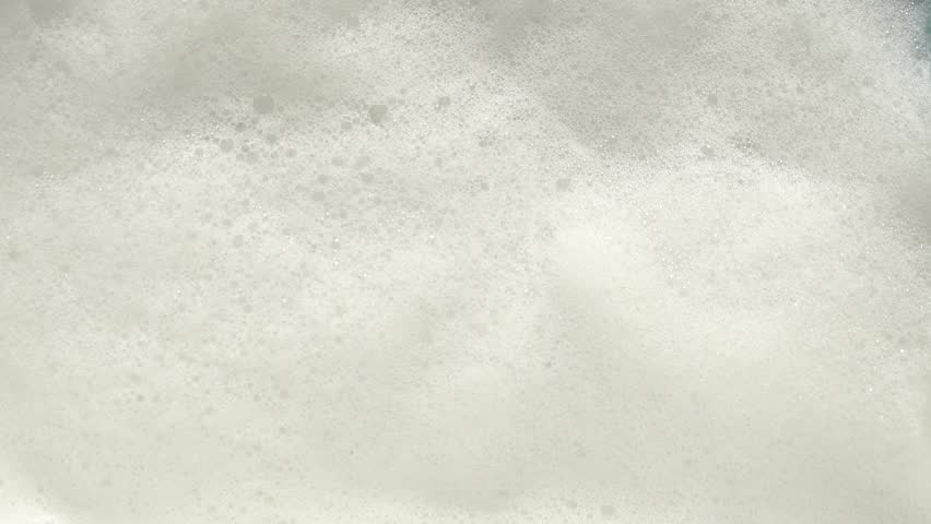 Foamy Surface of Bathing Water. White Foam on the Water. Foamed Detergent, Bubble Bath or Soap. Fine Air Bubbles on the Surface of White Bath Foam. The Gentle Ripple of Foamy Water.