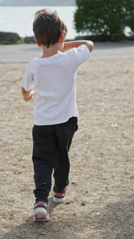 Bothered By The Sun, Little Boy Wipes Sweat From Face With His Arm During Park Walk With Lake And Mountains In The Background