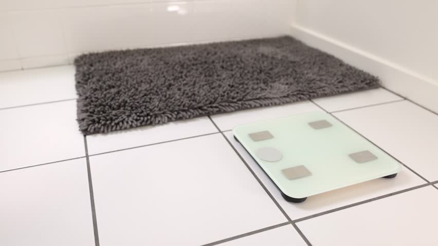 Woman checking her weight by stepping onto a bathroom scale.