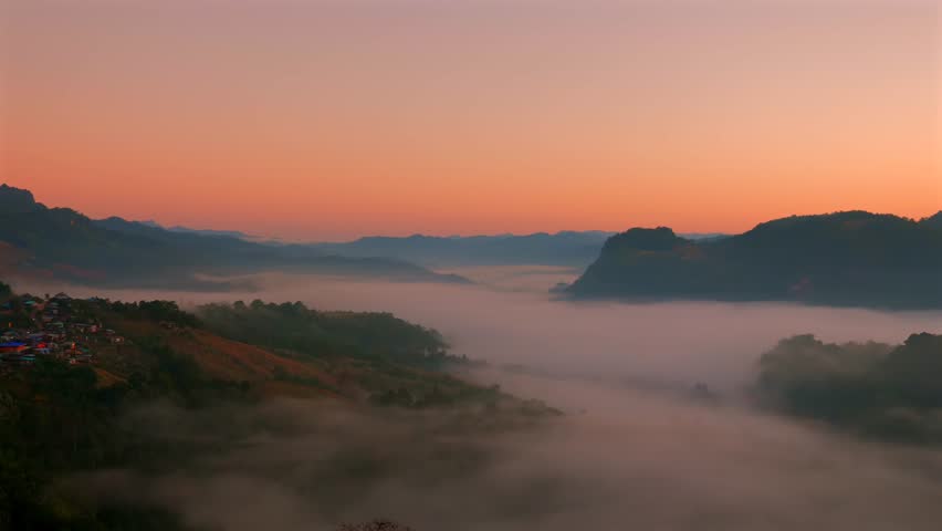 Sunrise landscape with mountains and valley blanketed in fog, showcasing natural tranquility and beauty in morning. Scenic view of foggy hills at dawn with warm light illuminating horizon.