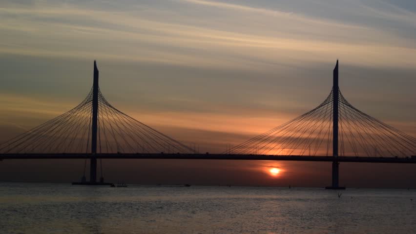 Full HD video. Sailboats sail on water of  Gulf of Finland. Bay. Cable-stayed bridge in Saint Petersburg. Russia. Sunset sky. Cars drive across bridge. Evening sun. Neva river. Cityscape. Keep calm