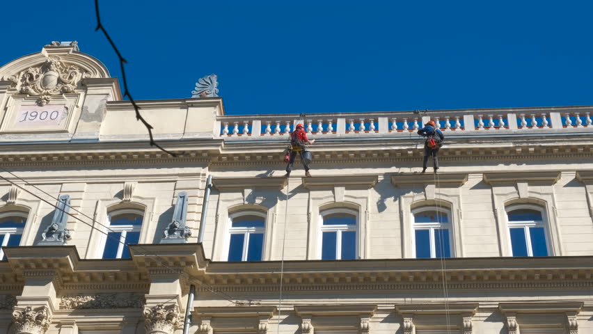 Professional cleaning on ancient building. A view of workers in uniform and helmet cleaning the building exterior on high in the city.