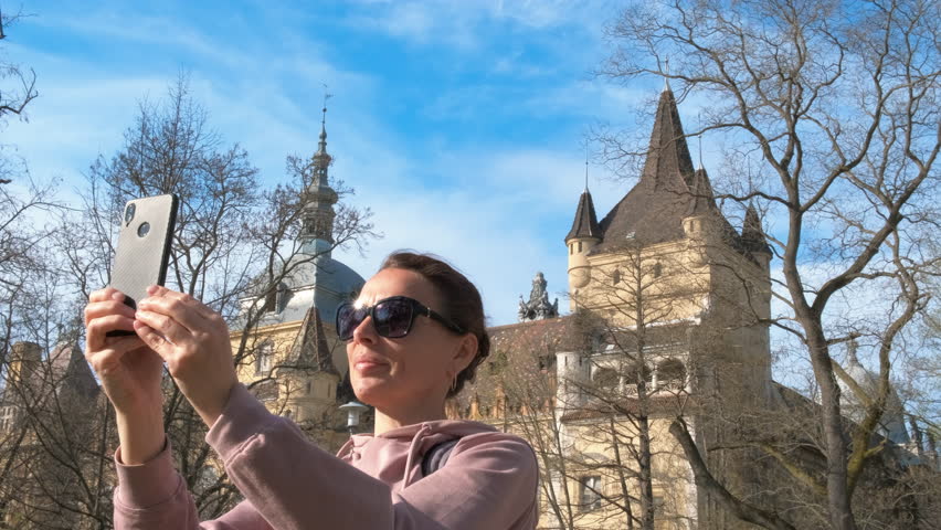 Female relaxing by budapest hungary castle. A happy woman in sunglasses taking selfie against Budapest castle in the sunny park.