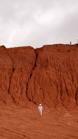 Drone out shot of an astronaut walking on red surface of far planet. Unknown far universe place with no acid rains and cosmic landscapes. Vertical Shot.