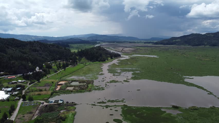 Drone aerial view over lake and grass area near houses and road blue sky tree area mountains background Colombia, Latin America 4k