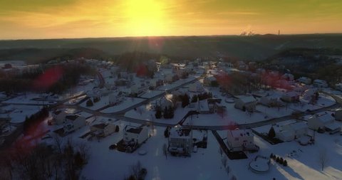 A slow forward winter sunset aerial establishing shot of snow covered roads and homes in a rust belt upscale residential neighborhood. Factory smokestacks in the distance. Pittsburgh suburbs.	 	