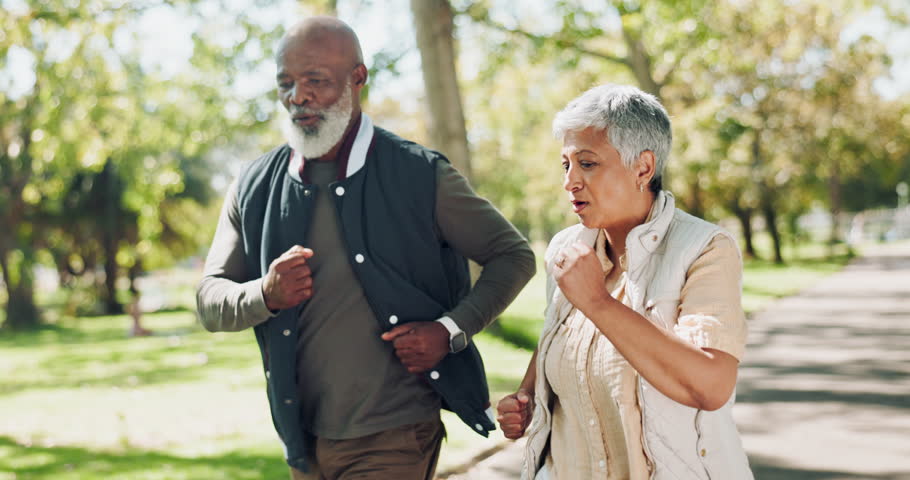 Interracial, senior couple and walking with partner in park for fitness, workout or cardio exercise. Man and woman in nature, road or street of woods for outdoor training, health and wellness