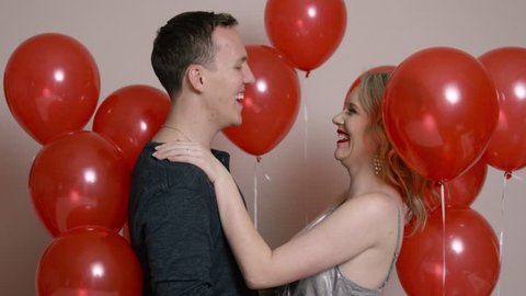 Happy Couple Surrounded by Red Balloons Laughing and Kissing