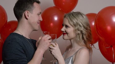 Happy Couple Surrounded by Red Balloons Drink Champagne and Kiss