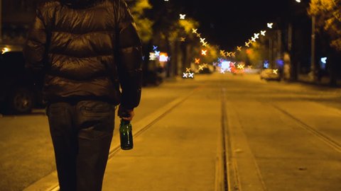 Drunk Man is Walking by the Night Carriageway Street and Drinking Beer form the Bottle