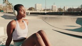Close-up side view of young athletic woman sits in a skatepark on a hot summer day, with skateboarders performing tricks in the background, enjoys the music - Powered by Shutterstock - Get 15% off with code: PIKWIZARD15