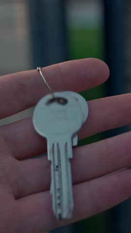 Hand of woman holds keys walking in yard to luxury triangle-shaped house with big panoramic windows. Ownership of mansion in countryside closeup Vertical Shot.