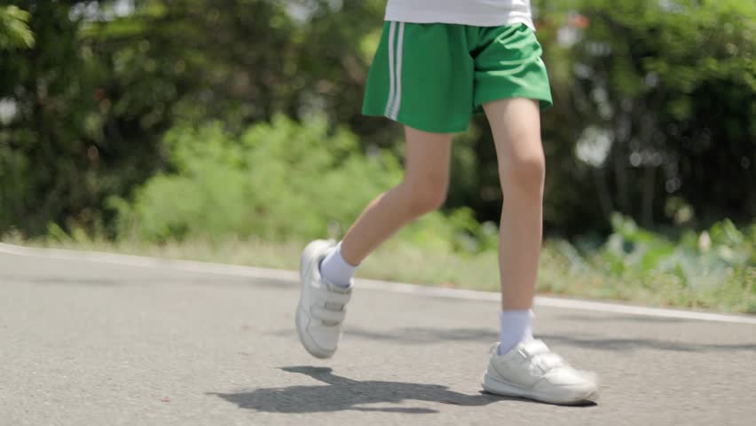 Asian Thai kid girl, aged 8 to 10 years, cute and beautiful face. She is jogging in the outdoor park. She is a girl with a good figure and is tall. Exercise makes her strong. background is green tree.