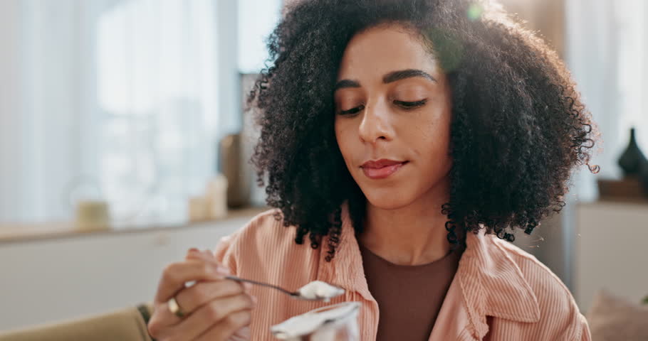Happy, woman and eating yogurt with spoon on sofa for healthy food, nutrition and balanced diet at home. Female person, detox and weight loss with snack or dessert alternative on couch for wellness