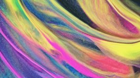 A close-up of swirling rainbow-colored ink in water, creating an abstract pattern with glitter and sparkle effects. The video background is a mix of neon colors, providing space for design elements