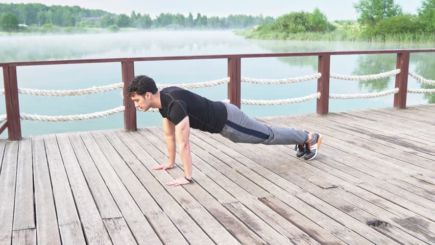 Young sporty man training on nature. Push up and plank close to the foggy lake	