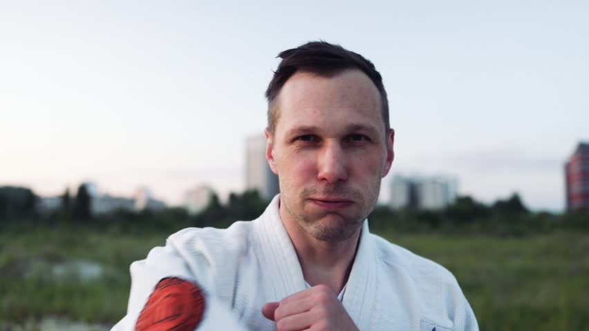 Karate athlete practicing kicks wearing kimono at Glade in City Park. Sporty man training martial arts. Active sportsman improve fighting skills outdoors. Sport concept.