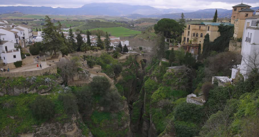 Ronda houses in old town on stone cliffs and bridge with flowers static shot