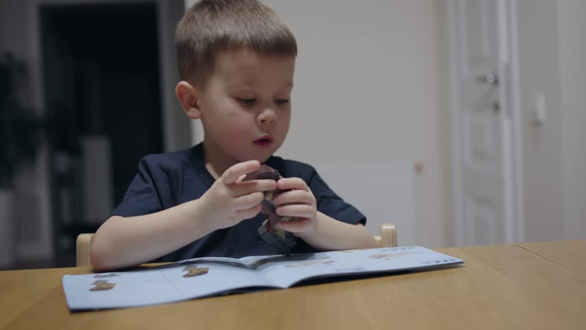Sitting at table young child playing toy constructor following instructions. Child playing with blocks bricks and cubes construct new toy following instructions colorful world of toy constructor set