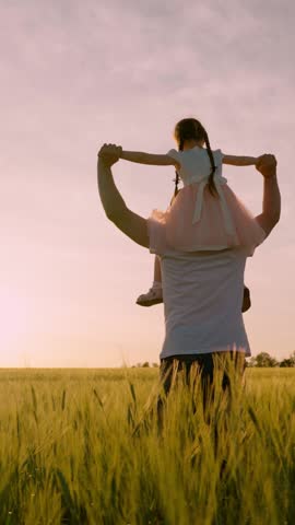 Child girl, dad travel on field. Happy child father are playing in field of ripening wheat. Little daughter on fathers shoulders. Kid, parent play in nature. Happy family child concept. Family holiday