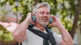 Joyful relaxed overjoyed mature bearded man listening favorite energetic disco rock n roll music dancing outdoors. Adult guy taking off wireless headphones looking at camera smiling on city street. - Powered by Shutterstock - Get 15% off with code: PIKWIZARD15